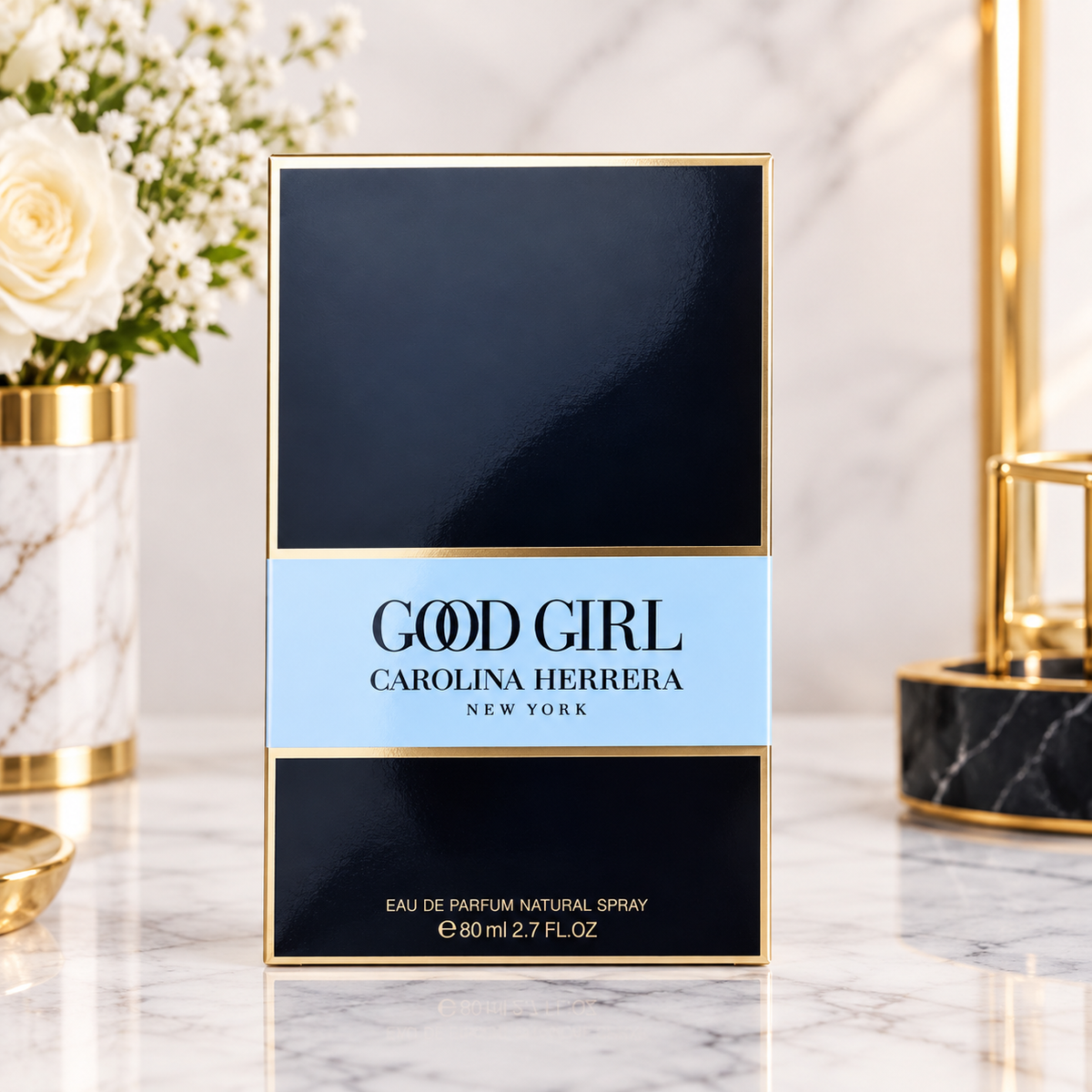 Carolina Herrera Good Girl Eau de Parfum box, 90ml, standing on a marble surface with a white rose in a gold-rimmed vase on the left and a gold lamp on the right.