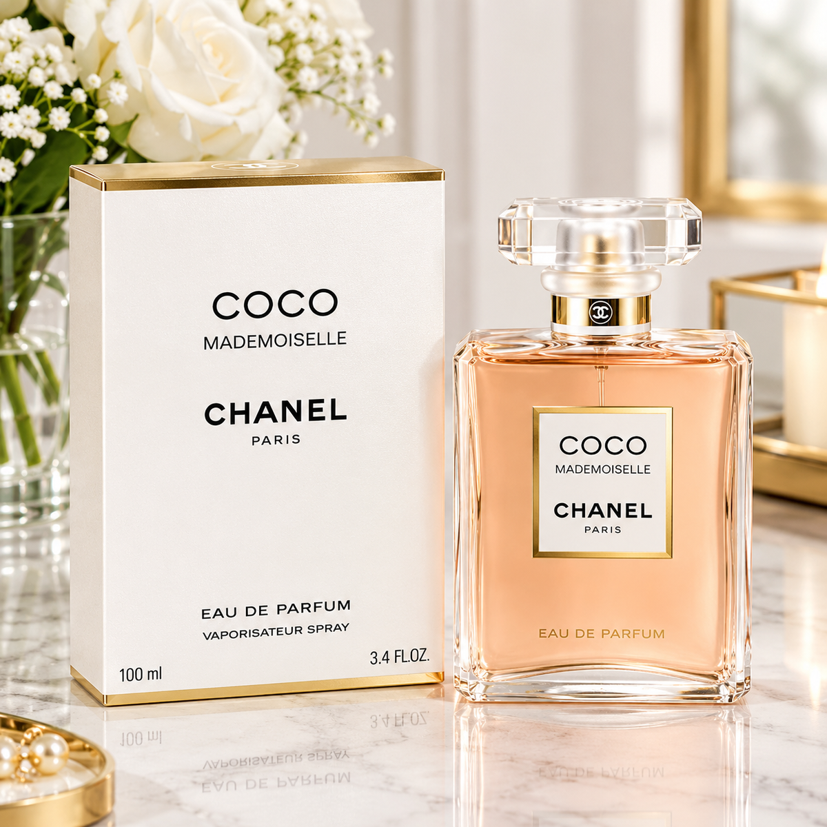 Chanel Coco Mademoiselle Eau de Parfum shown with its white and gold box and the clear glass perfume bottle filled with peach-colored fragrance, set on a marble surface with flowers in the background.