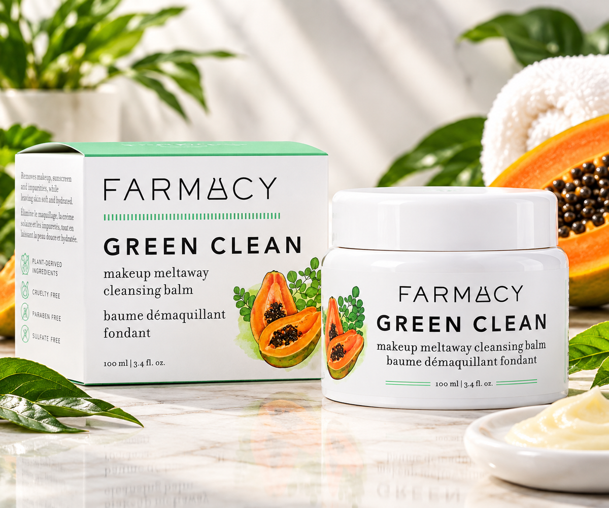 FARMACY Green Clean makeup meltaway cleansing balm shown with its white and mint-green product box and a white jar, styled on a marble surface with papaya, leaves, and a towel in the background.