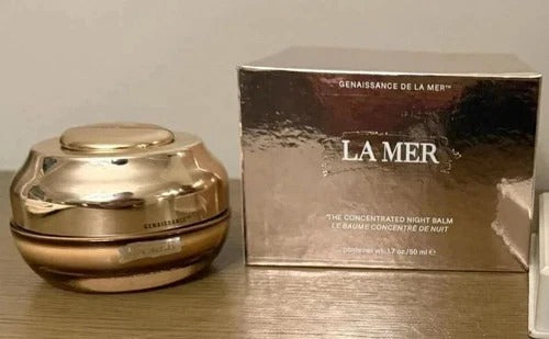 La Mer The Concentrated Night Balm jar in a reflective metallic gold finish, shown next to its matching metallic gold outer box on a wooden surface.