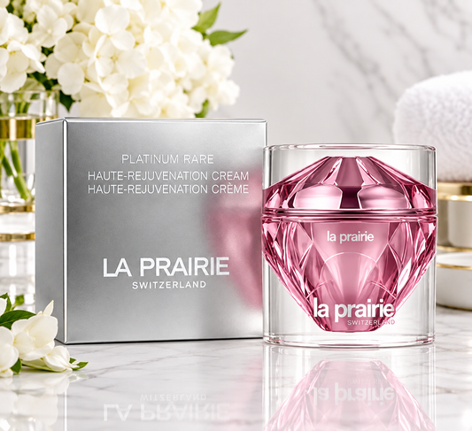 La Prairie Platinum Rare Haute-Rejuvenation Cream shown with its silver box and a faceted pink cosmetic jar on a marble surface with white flowers in the background.